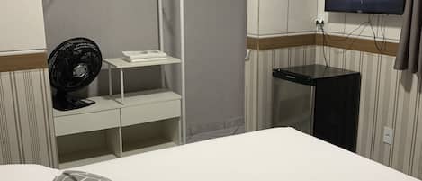 Una habitación de hotel con una cama, un televisor montado en la pared, un ventilador y una mesita.