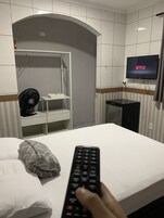 Una habitación de hotel con una cama, un televisor montado en la pared, un ventilador y una mesita.