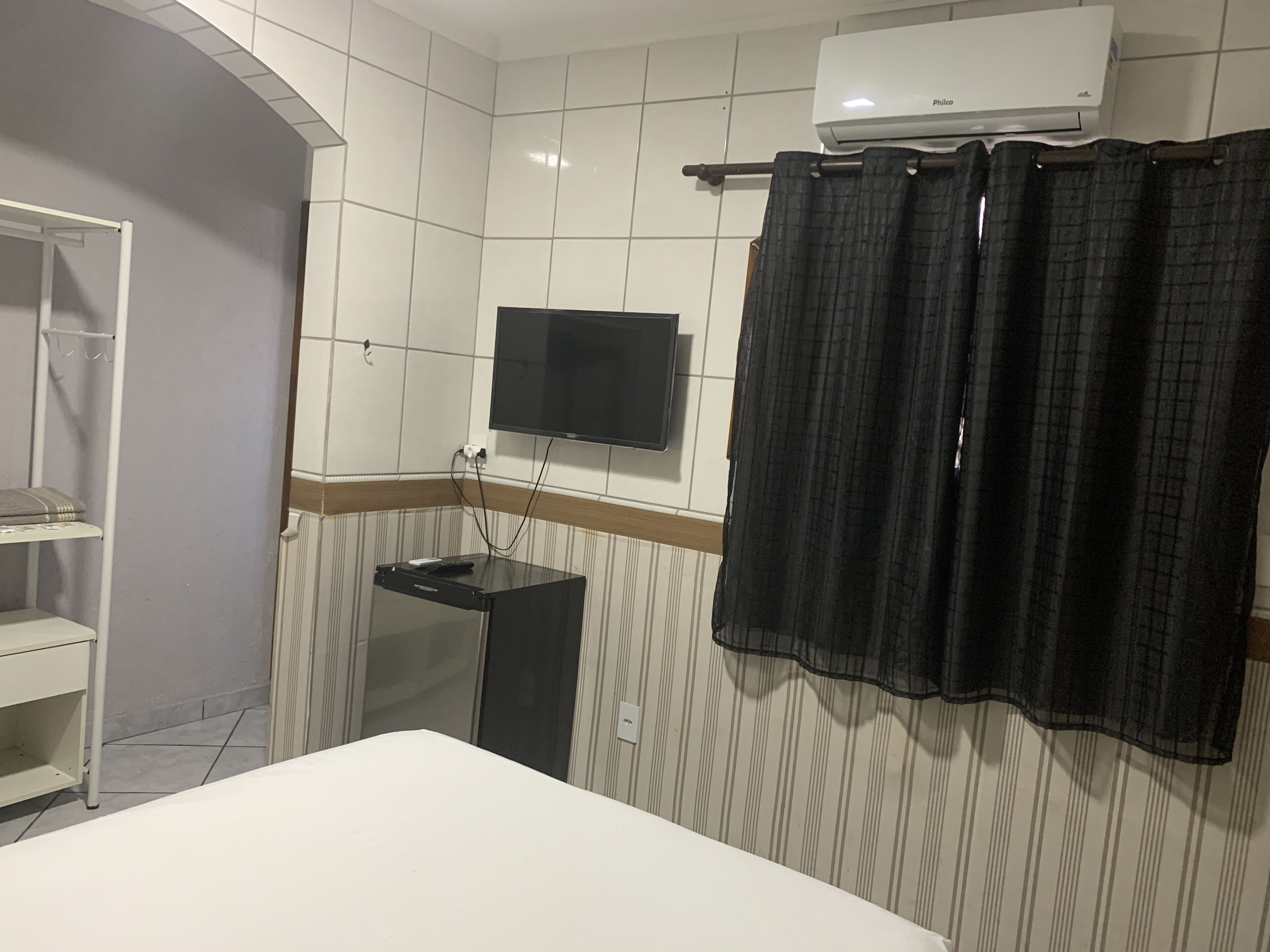 A hotel room with a bed, a TV mounted on the wall, a small table, a shelf, and a shower curtain.