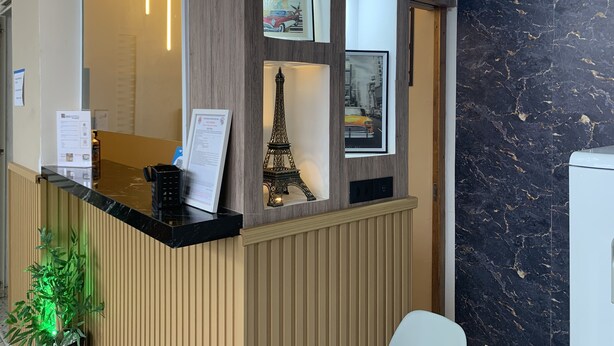 A reception desk with a black marble top, framed pictures including the Eiffel Tower, and a wooden panel design. - Pousada EAS GRU Airport (Guarulhos)