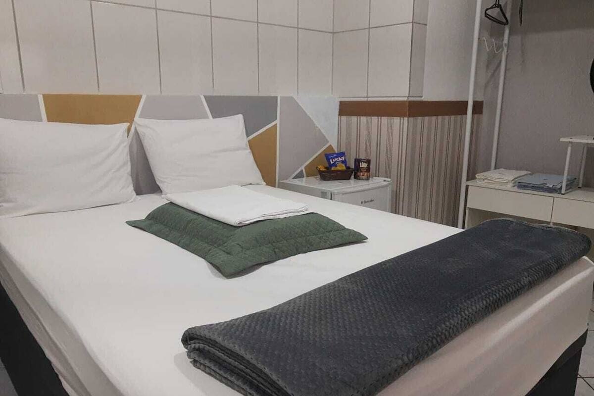 A neatly made bed with white and green pillows, a folded blanket, and a bedside table with a lamp and a small box.