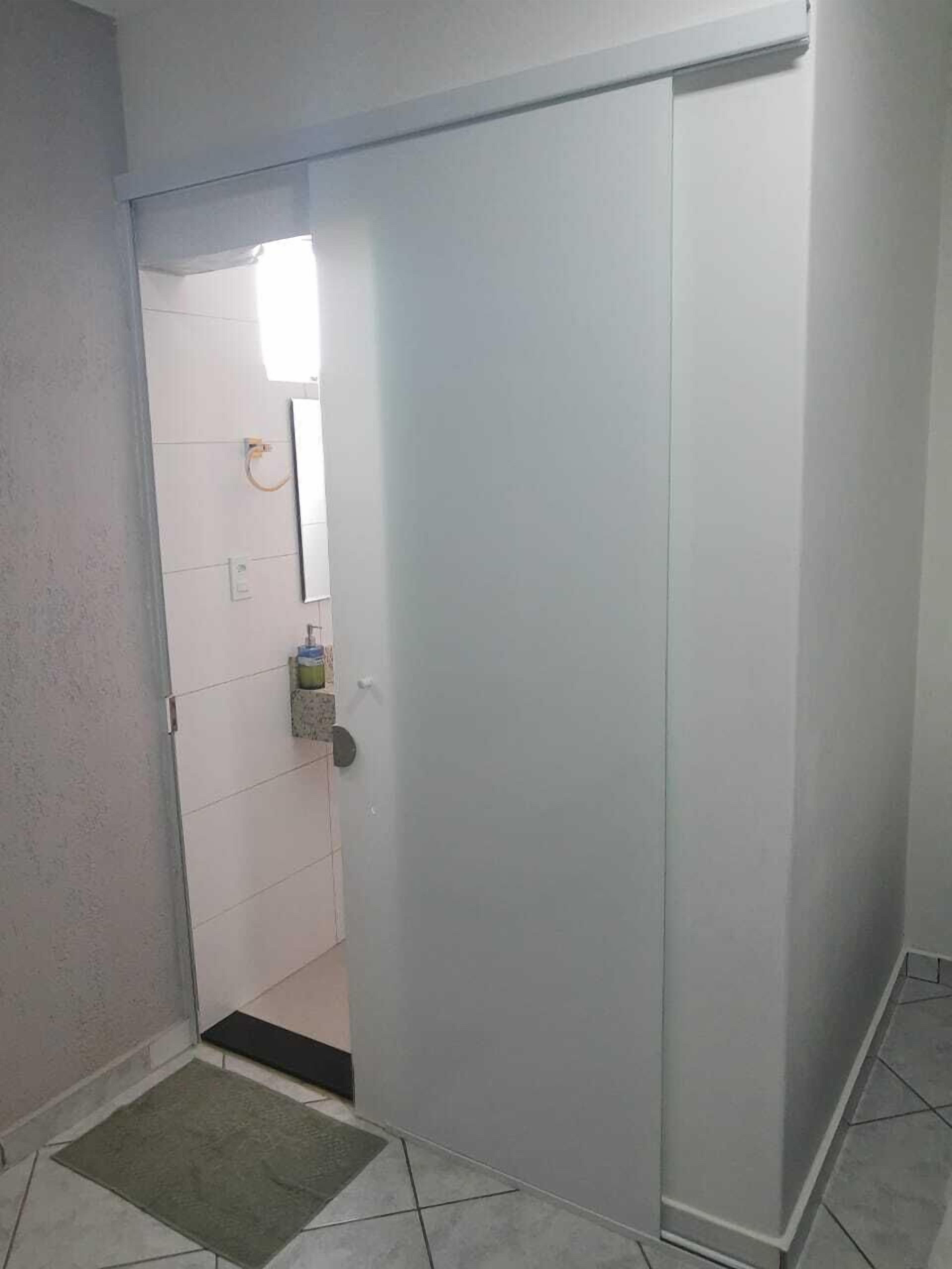 A room with a sliding door leading to a bathroom. The bathroom has a toilet, a sink, and a mirror. There is a small rug on the floor near the door.