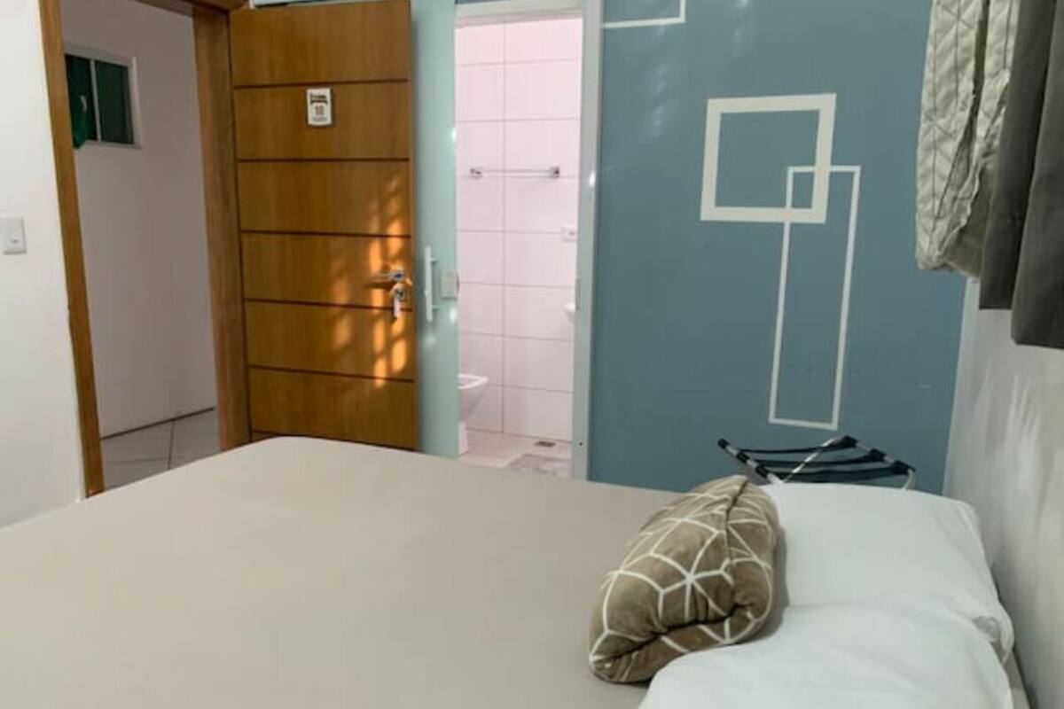 A hotel room with a bed, a wooden door, and a bathroom visible through an open door.
