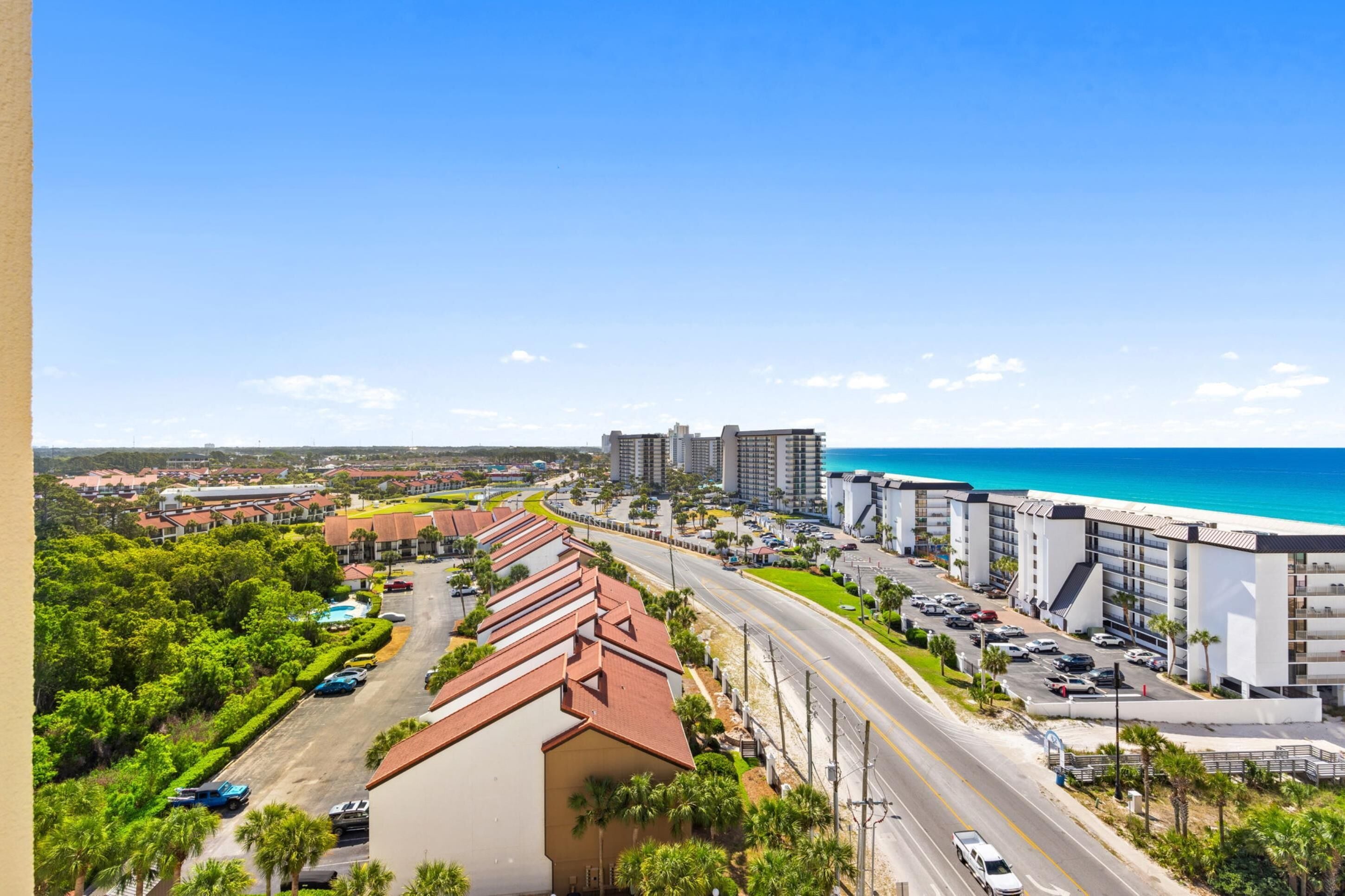 A coastal hotel with a parking lot, a road, and a view of the ocean.