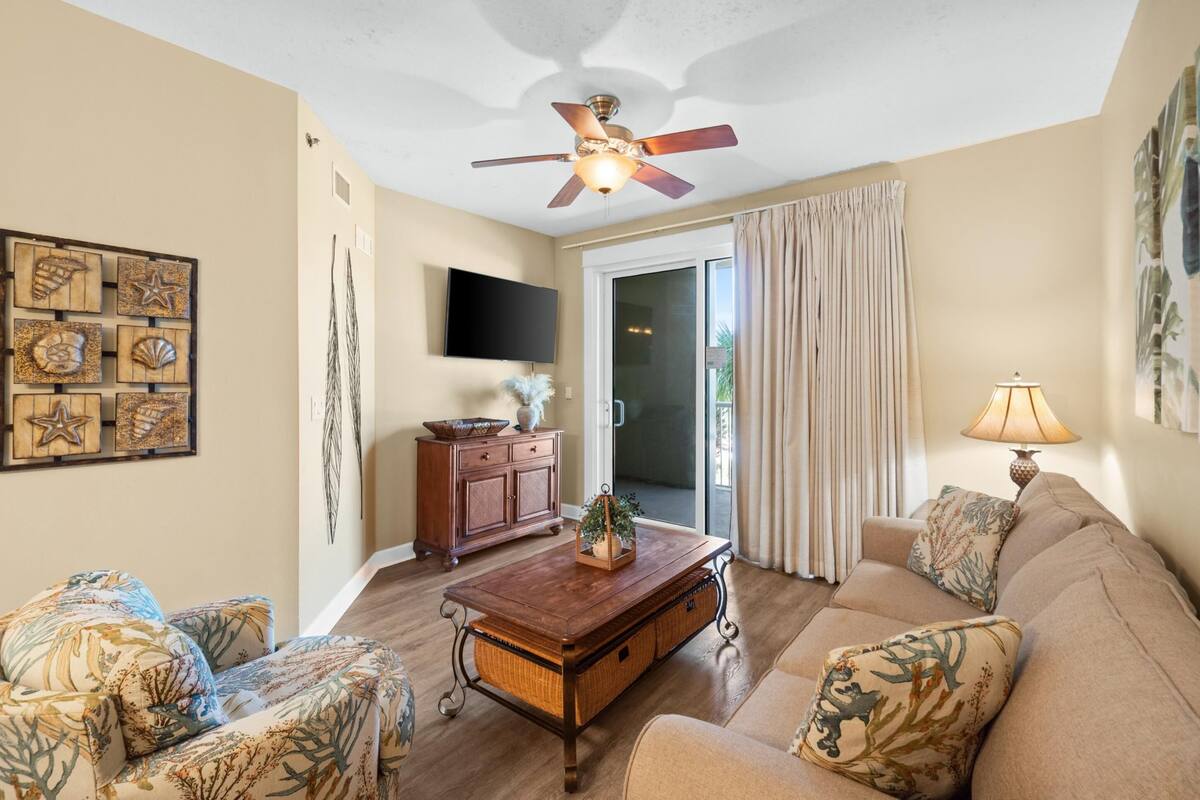 A living room with a ceiling fan, a wooden coffee table, a sofa, and a television mounted on the wall.