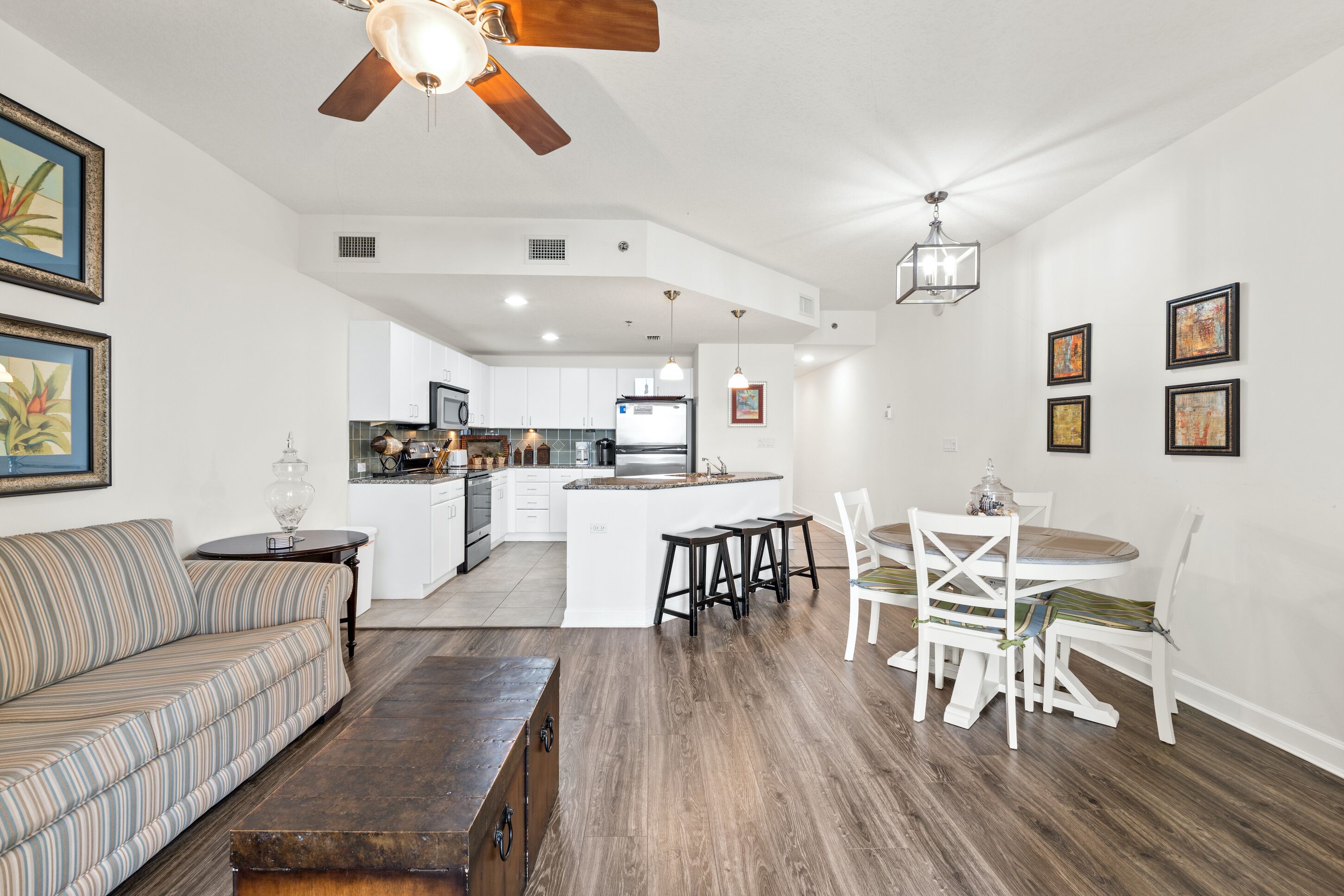 A spacious living area with a sofa, coffee table, dining table with chairs, and a kitchen in the background.