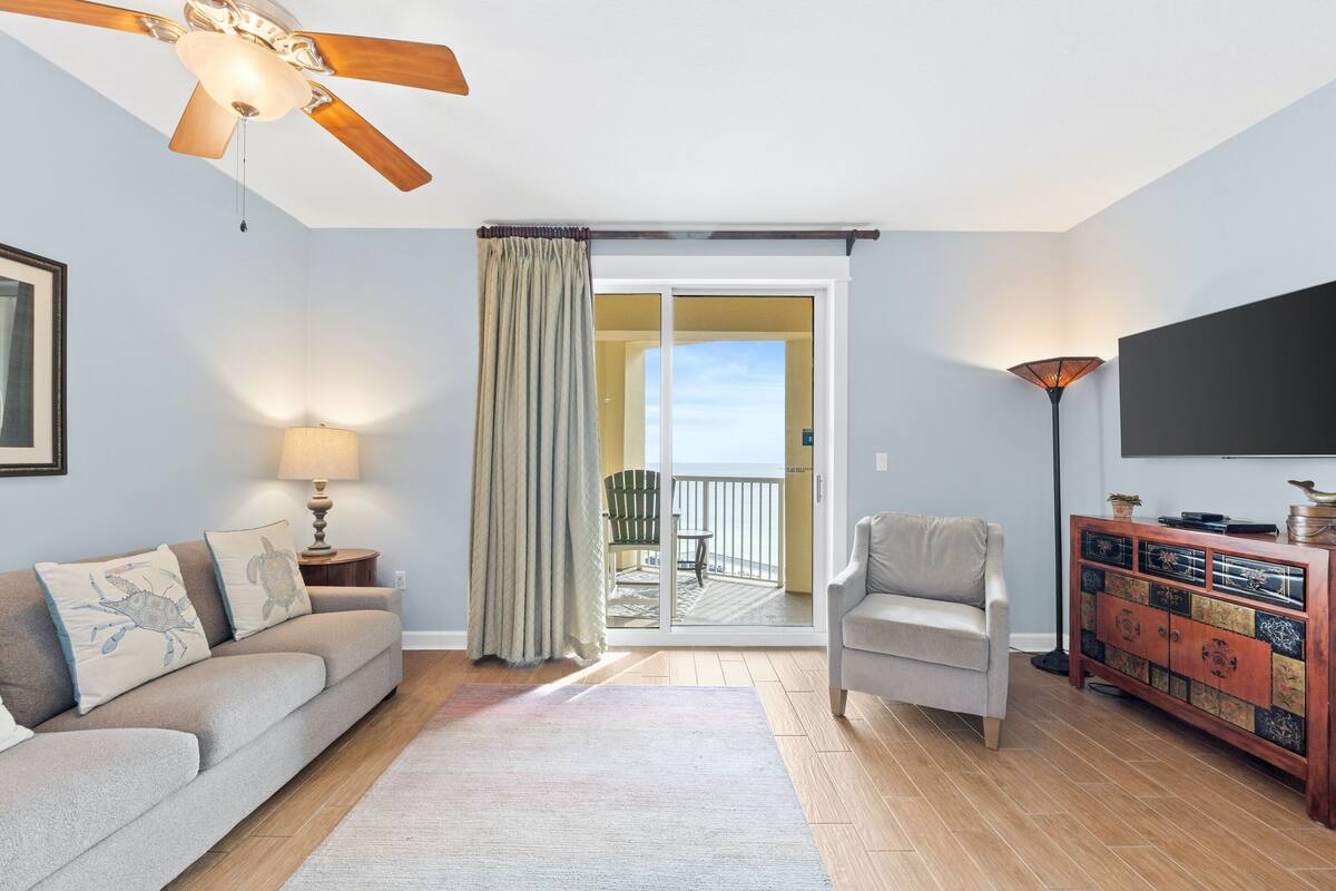 A living room with a sofa, a chair, a TV, a ceiling fan, a lamp, a cabinet, and a sliding glass door leading to a balcony.