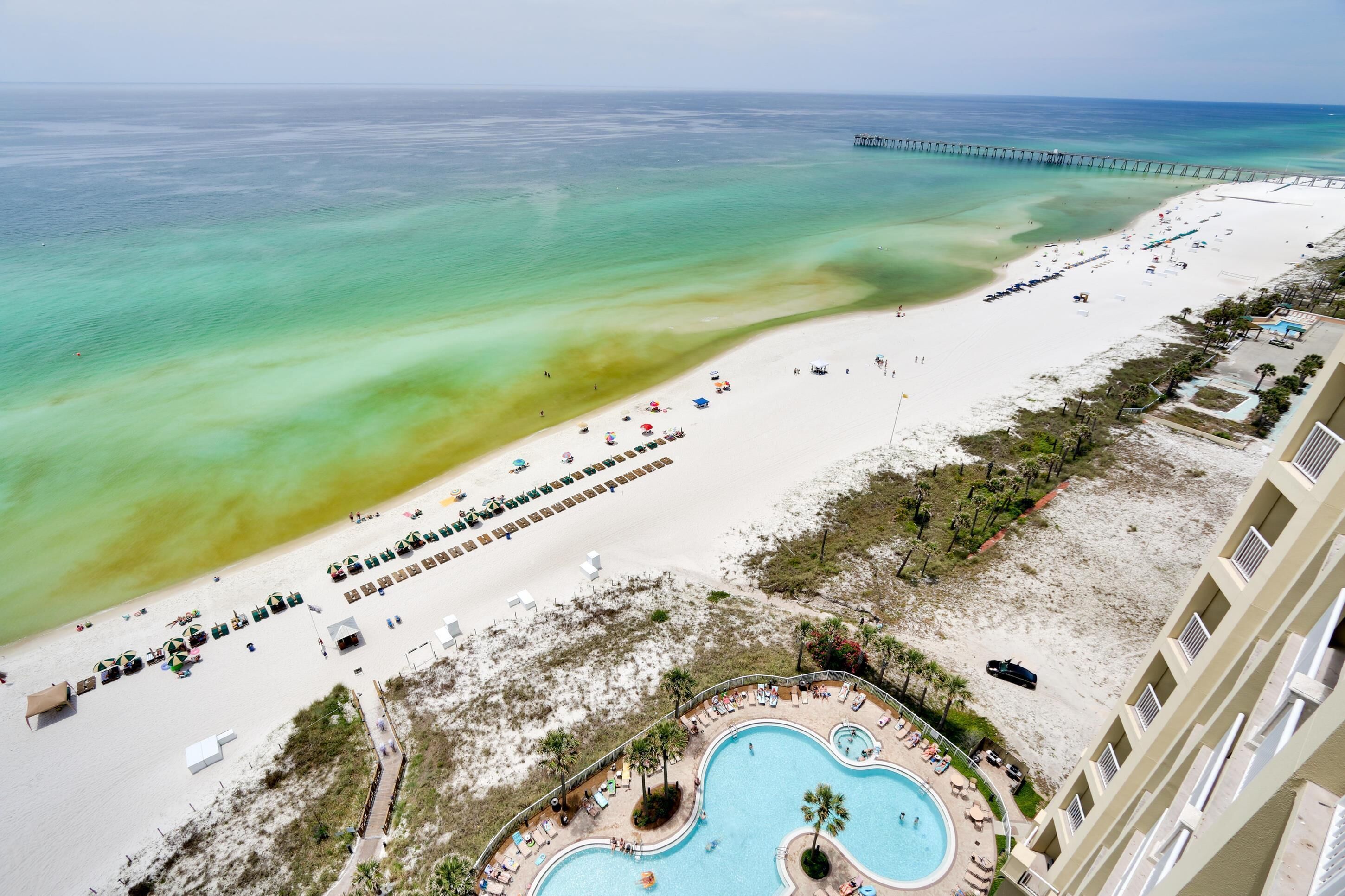 Un resort en la playa con piscina, sombrillas y un muelle.