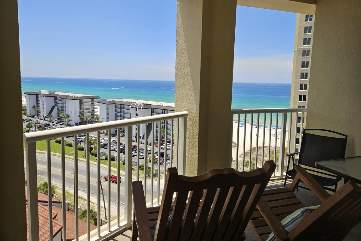 A balcony with a view of the ocean and a parking lot.