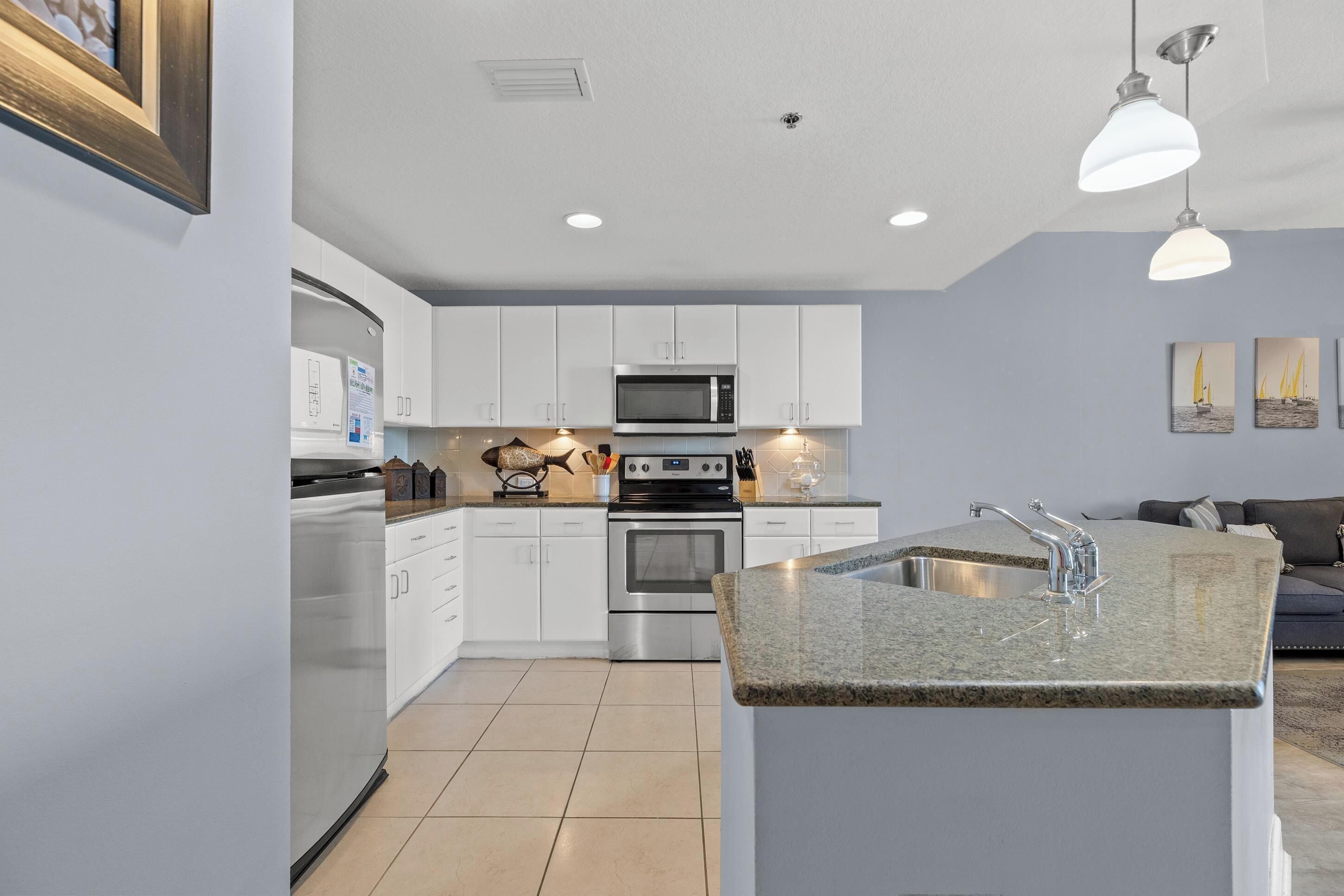 A modern kitchen with white cabinets, a stainless steel oven, a microwave, and a granite countertop island with a sink.