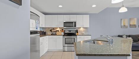A modern kitchen with white cabinets, a stainless steel oven, a microwave, and a granite countertop island with a sink.