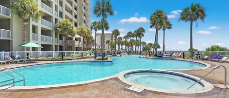 A hotel pool area with multiple swimming pools, palm trees, and lounge chairs.