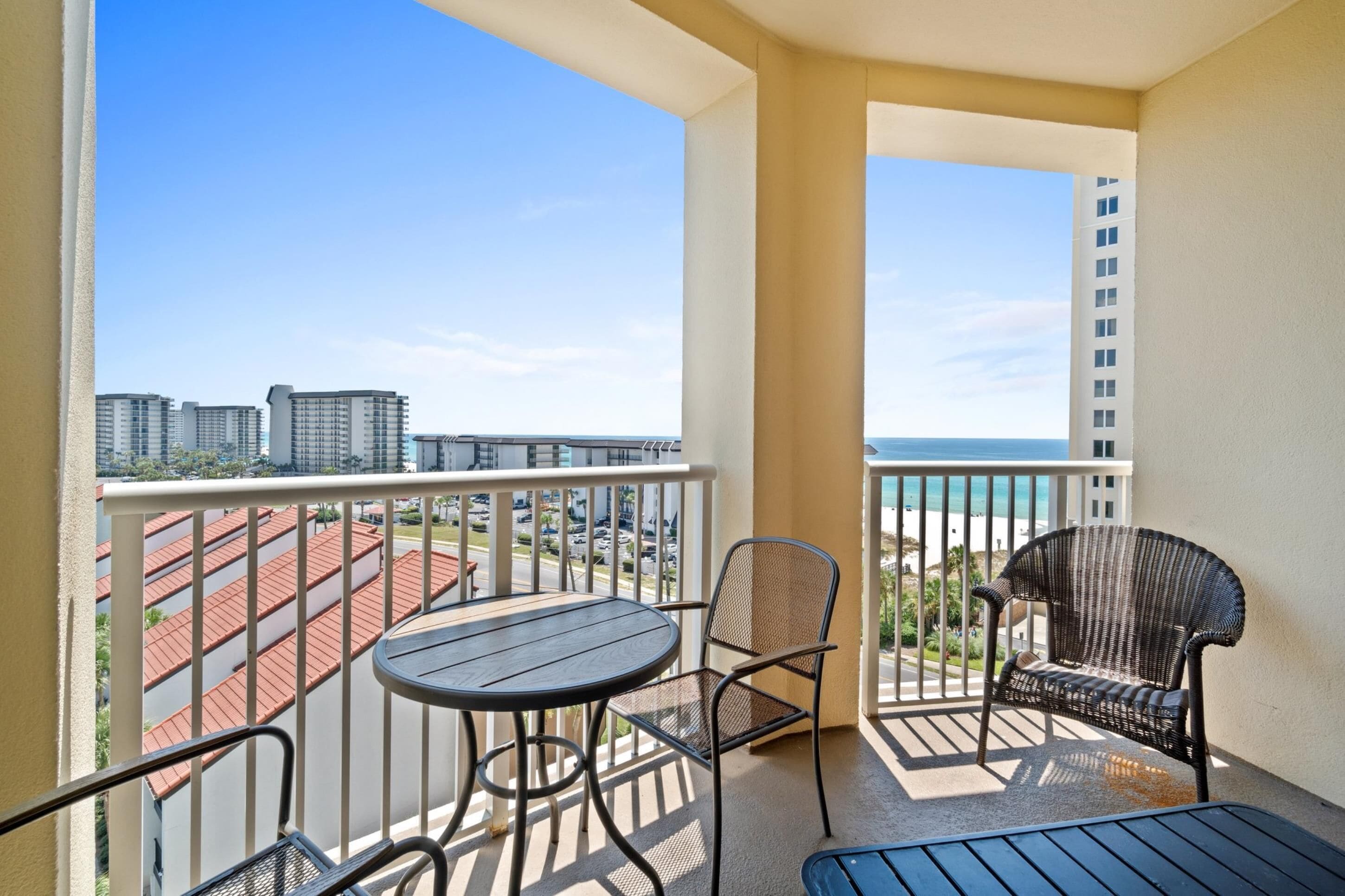 Un balcón con mesa y sillas, con vista a un paisaje urbano y una playa.