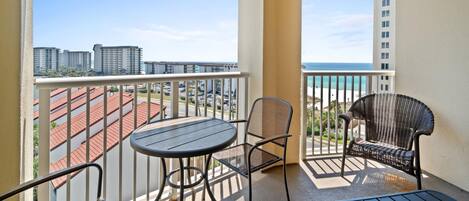 Un balcón con mesa y sillas, con vista a un paisaje urbano y una playa.