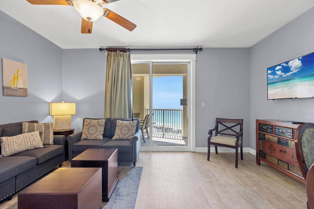 A living room with a sofa, coffee table, TV, and a view of the balcony.