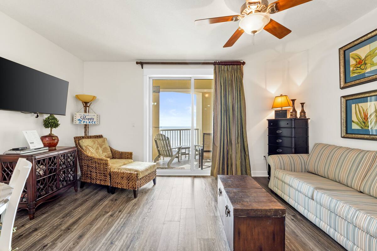A living room with a television, wicker chair, sofa, wooden coffee table, and a ceiling fan.