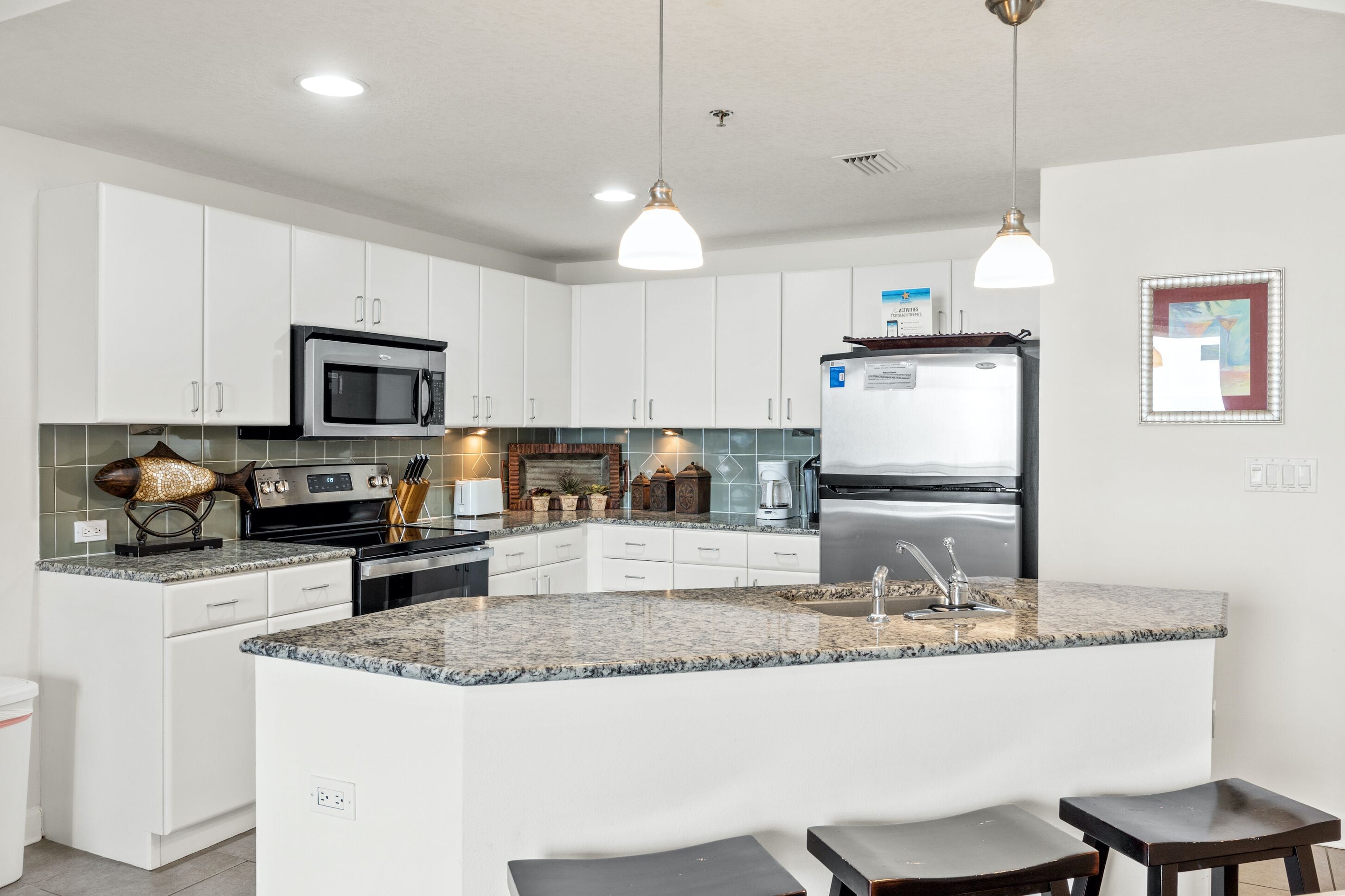 Une cuisine moderne avec des armoires blanches, des comptoirs en granit, des appareils en acier inoxydable et des luminaires suspendus.
