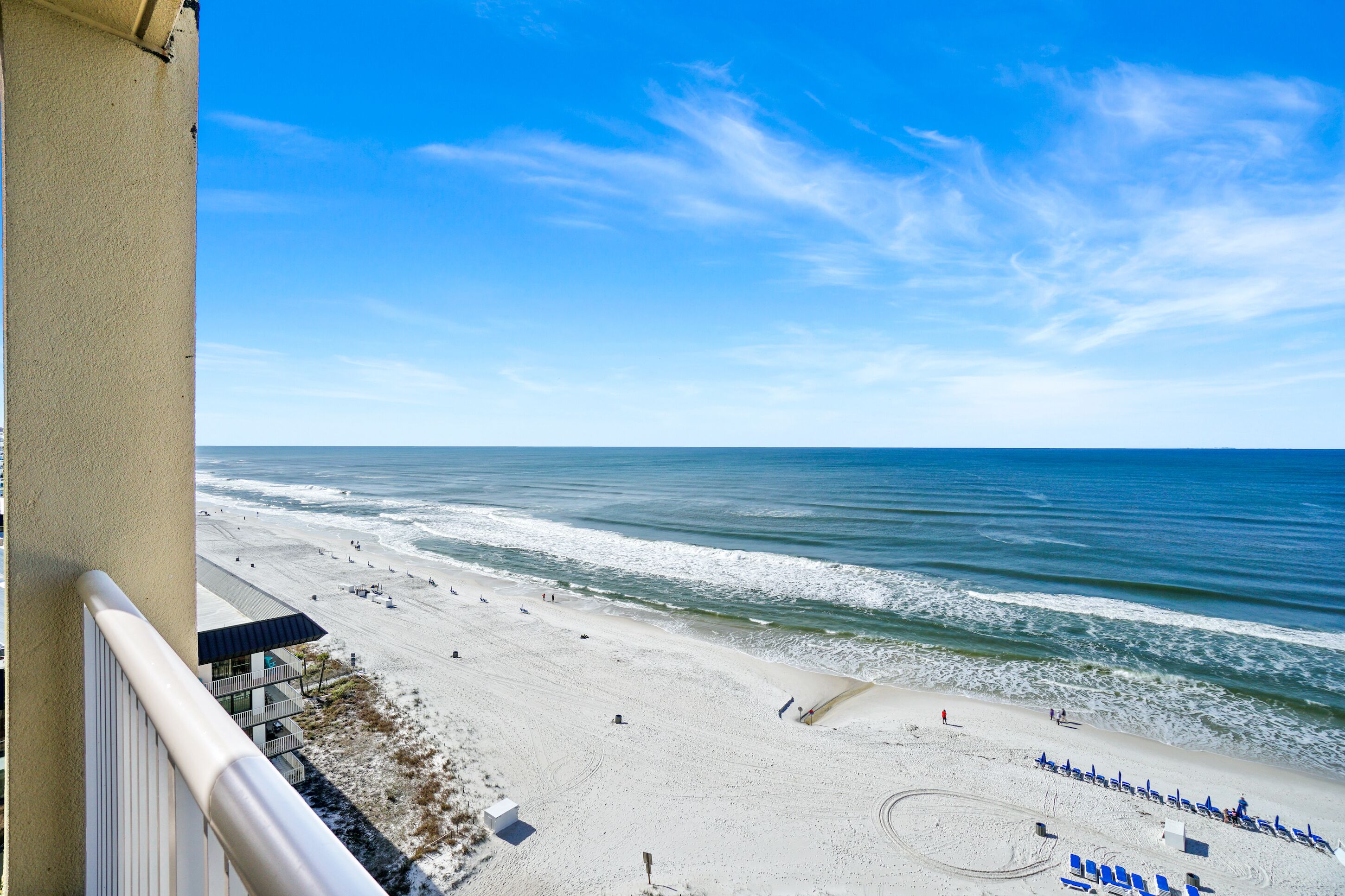 A beach view from a balcony with a clear sky, sandy beach, and ocean waves.