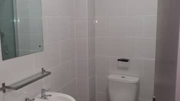 A small, modern bathroom with white tiles, a glass shelf above the sink, and a toilet with a flush handle.