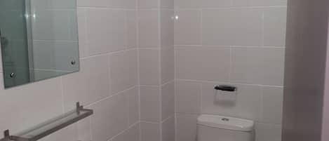 A small, modern bathroom with white tiles, a glass shelf above the sink, and a toilet with a flush handle.