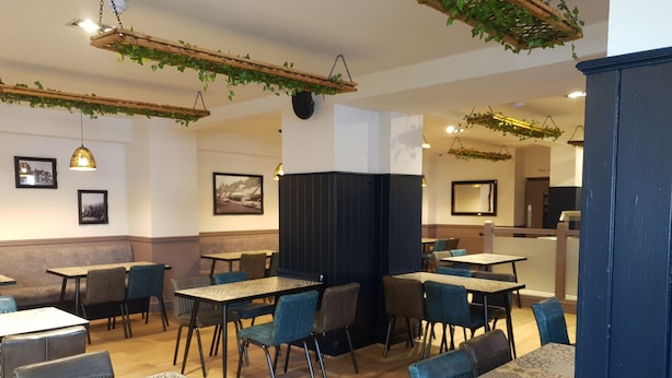 A restaurant with booths and tables, wooden flooring, hanging plants, and framed pictures on the walls. - The Bournbrook Inn (Birmingham)