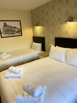 A hotel room with two beds, a nightstand, a lamp, and a framed picture on the wall.