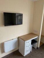A room with a white desk, a black TV mounted on the wall, and a white radiator.