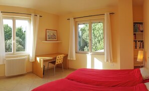 Une chambre à coucher avec un lit, un bureau et deux fenêtres avec des rideaux.