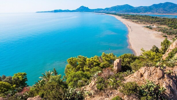 Un paysage côtier avec une plage, une mer d’un bleu limpide et une végétation verdoyante.