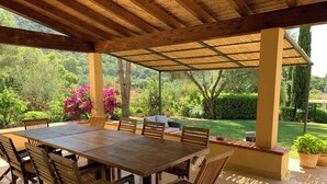 Une terrasse couverte avec une table et des chaises en bois, entourée d’une végétation luxuriante et offrant une vue sur le paysage.