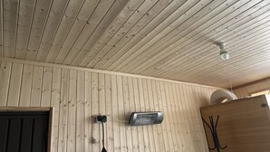 A room with a wooden ceiling and walls, a ceiling fan, a wall-mounted heater, and a door.