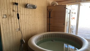 A wooden interior with a hot tub, a heater, and a door leading outside.