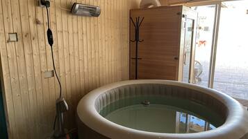 Un intérieur en bois avec un bain à remous, un chauffage et une porte donnant sur l’extérieur.