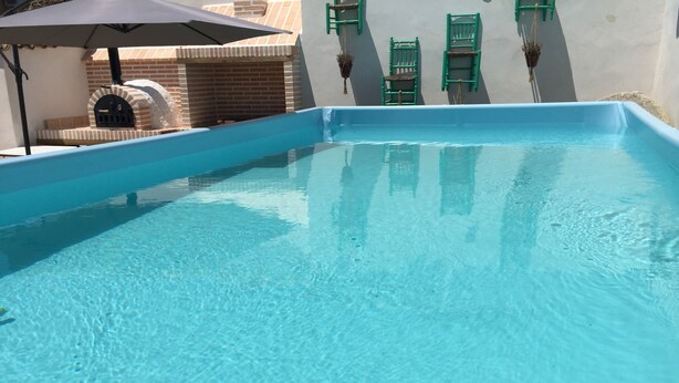 A clear blue swimming pool with a brick structure and green chairs.