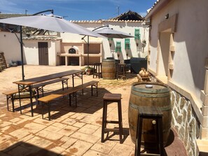 Un espace extérieur aménagé en terrasse, avec un sol en briques, des bancs en bois et un grand parasol pour créer de l’ombre.