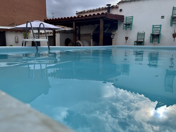 Une piscine offrant une vue dégagée sur les bâtiments environnants et un espace abrité avec un fauteuil.