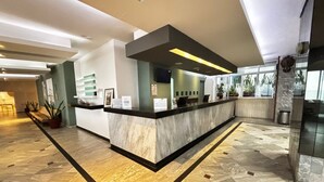 A modern reception area with a marble counter, potted plants, and a seating area with a bench. - Hotel Royalty (Veracruz)