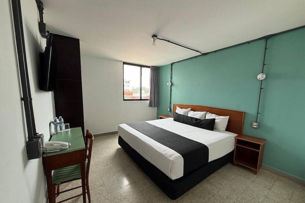 Une chambre d’hôtel avec un lit, un bureau, une chaise, un téléviseur fixé au mur et une fenêtre.