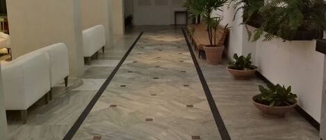 A spacious hallway with a patterned floor, seating areas, and potted plants.