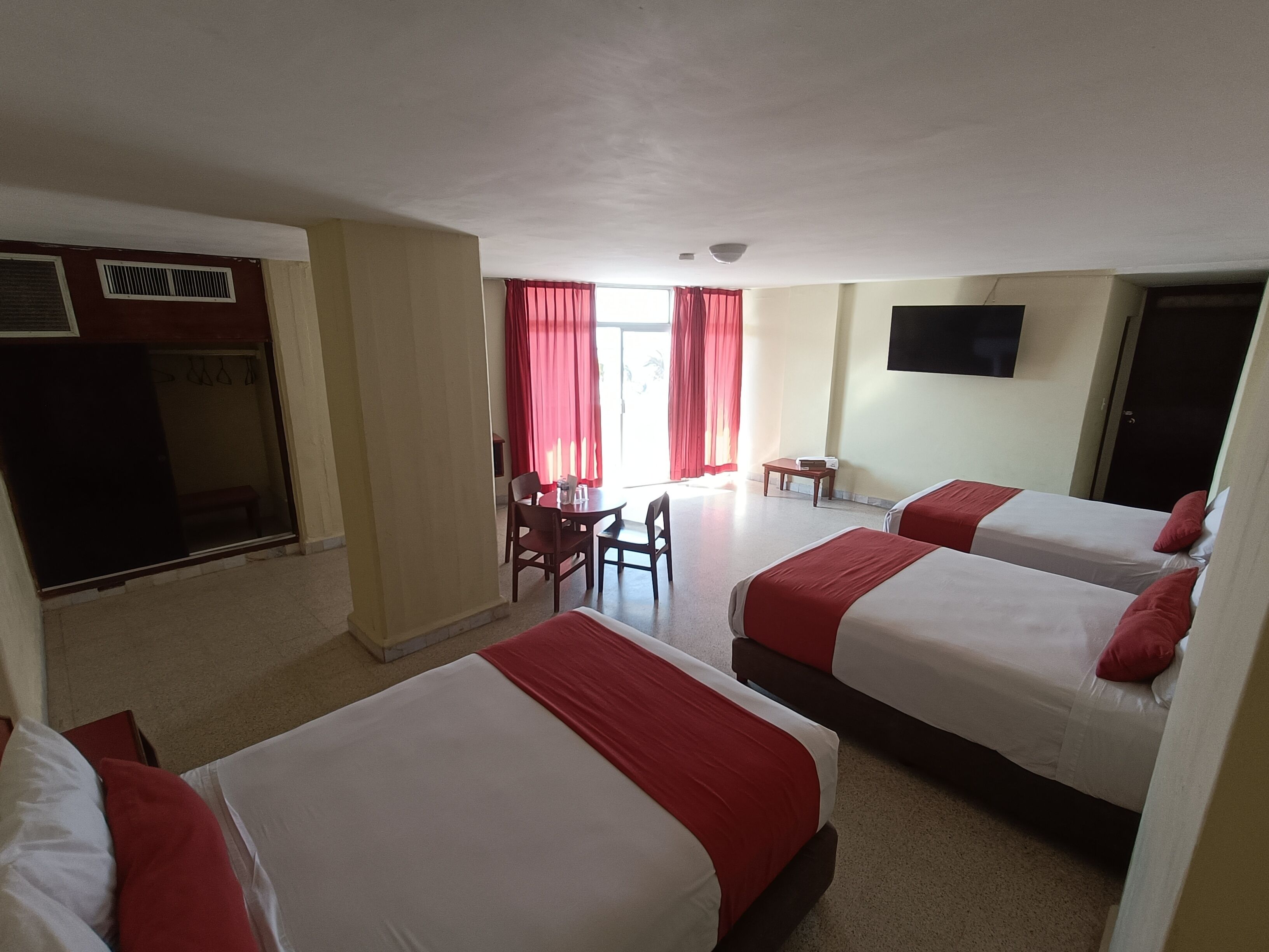 A hotel room with three beds, a desk, a chair, and a television on the wall.