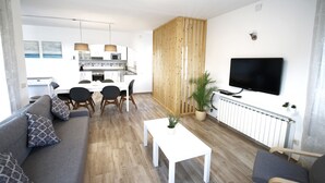 A modern living room with a sofa, coffee table, and TV. There is a dining area with chairs and a table, and a kitchen in the background. - Villa Paradis Costa Dorada (Miami Playa)