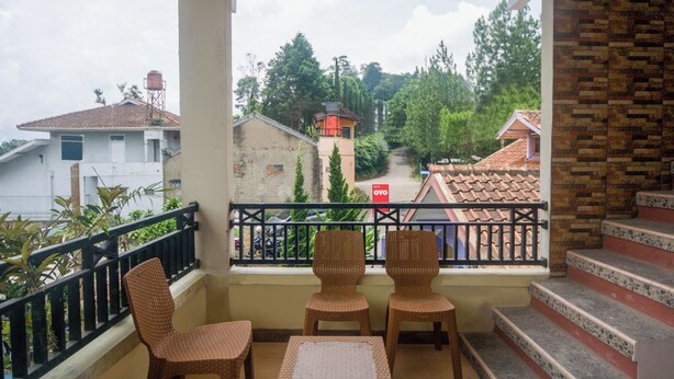 Un balcón con sillas de mimbre y una mesa, con vista a una zona residencial con casas y árboles.
