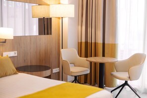Una habitación de hotel con una cama, dos sillas, una mesita, una lámpara y cortinas.
