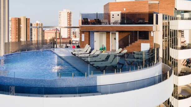 A rooftop pool with lounge chairs, a wooden deck, and a view of the city skyline. - Gold Arcos (Benidorm)