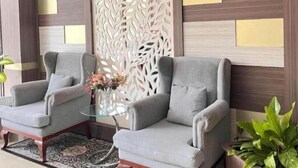 Two grey armchairs with a glass coffee table between them, a decorative white panel, and a potted plant. - Hotel Mekkah Banda Aceh (Banda Aceh)