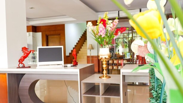 A reception desk with a laptop, a vase of flowers, and a red sculpture. - Hotel Mekkah Banda Aceh (Banda Aceh)