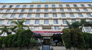 Un hotel de varios pisos con fachada plana, unidades de aire acondicionado y un toldo rojo sobre la entrada.