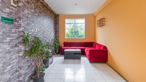 A modern living room with a red sofa, a coffee table, and potted plants. - OYO 3146 Emerald Hill (Karawang)