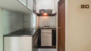 A compact kitchen with a built-in oven, a sink, and a dishwasher. - OYO 3146 Emerald Hill (Karawang)