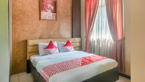 A hotel room with a bed, a headboard, a framed picture on the wall, and a window with curtains. - OYO 3146 Emerald Hill (Karawang)